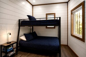 A bunk bed room with a window, a bedside table with a lamp, and a small shelf with items. - Luxury Cabin with Private Hot Tub & Sauna Getaway in Broken Bow, Oklahoma (Broken Bow)