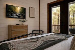 A bedroom with a bed, a dresser, a painting, and a window with a view of trees. - Luxury Cabin with Private Hot Tub & Sauna Getaway in Broken Bow, Oklahoma (Broken Bow)