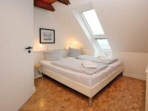 Ein Schlafzimmer mit schrägen Wänden, einem Bett mit weißer Bettwäsche, zwei Nachttischlampen und einem gerahmten Bild an der Wand.