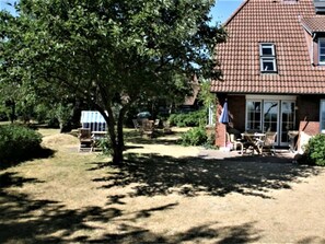 Ein Haus mit einem Ziegeldach, einer Terrasse mit Gartenmöbeln und einem Baum im Vorgarten.
