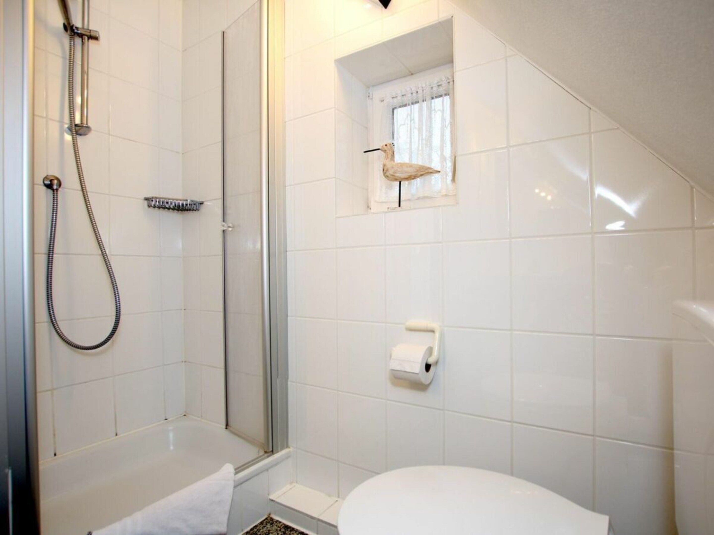 A bathroom with a shower, toilet, and a small window with a curtain.
