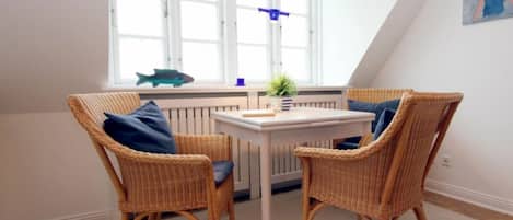 A room with two wicker chairs, a small table, and a window with a view of the outside.