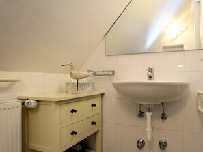 Ein Badezimmer mit weißem Waschbecken, einem Spiegel und einem Schrank mit Schubladen.
