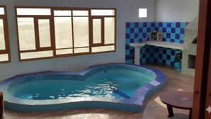 A swimming pool with a curved edge, a sink, and a tiled backsplash in a room with large windows. - Arabian Sea Hotel & Chalets - Two-Bedroom Chalet 2 (Aş Şulayb)