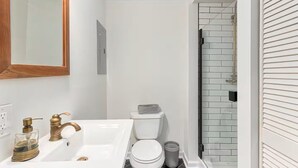 Ein Badezimmer mit einem weißen Waschbecken, goldenen Armaturen, einer Toilette und einer Duschkabine mit weißen Fliesen.