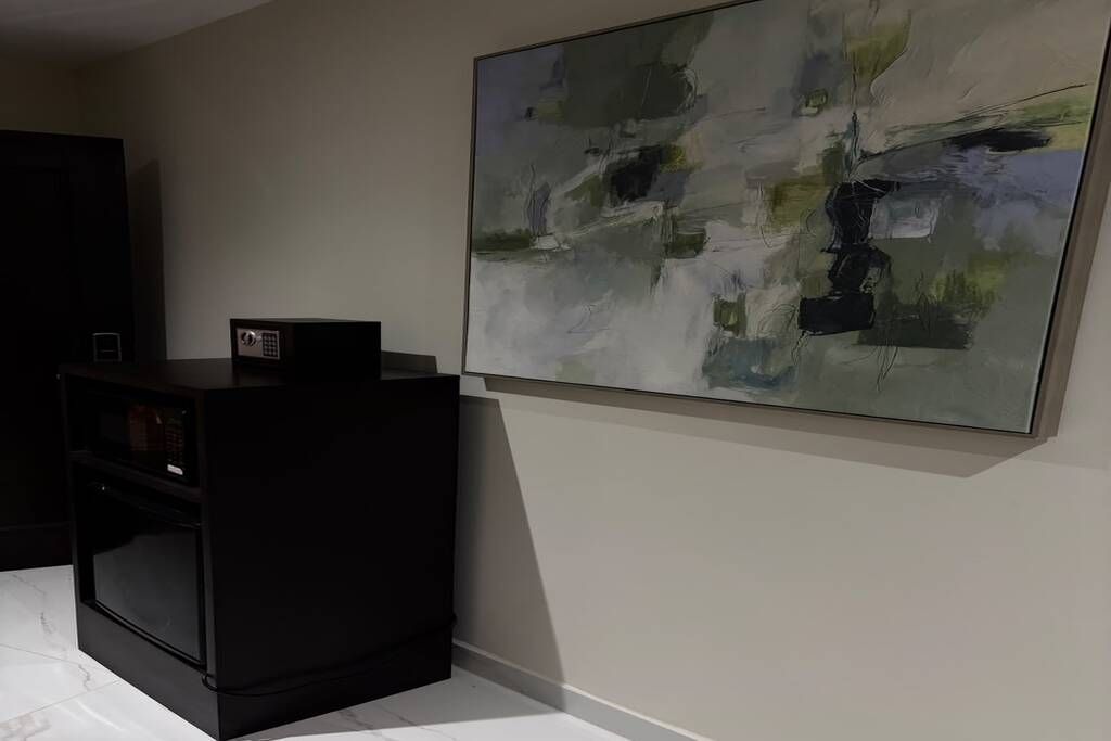 A room with a black cabinet, a large abstract painting on the wall, and a small electronic device on top of the cabinet.