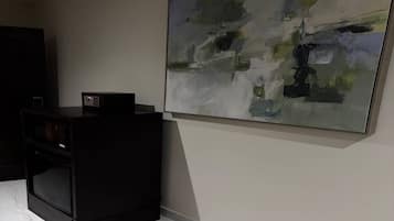A room with a black cabinet, a large abstract painting on the wall, and a small electronic device on top of the cabinet.