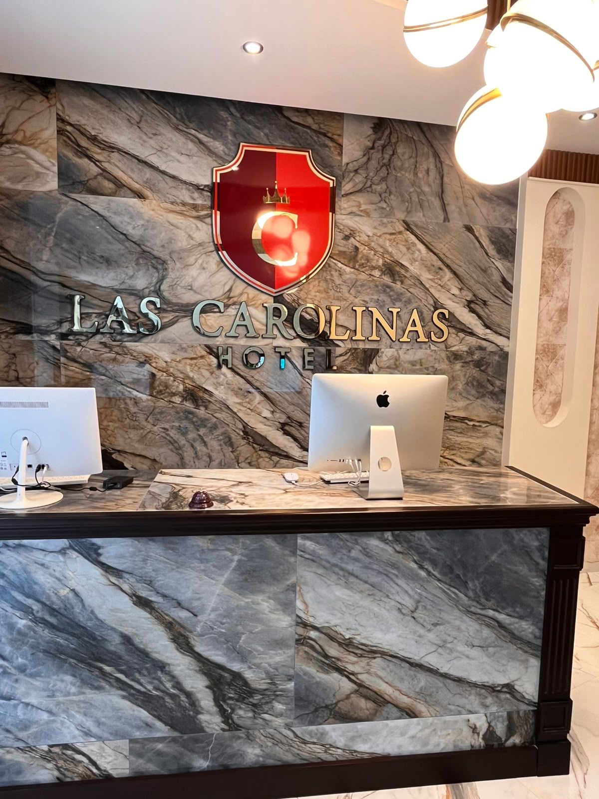 Una recepción con mostrador de mármol, dos computadoras Apple iMac y un cartel de hotel arriba.