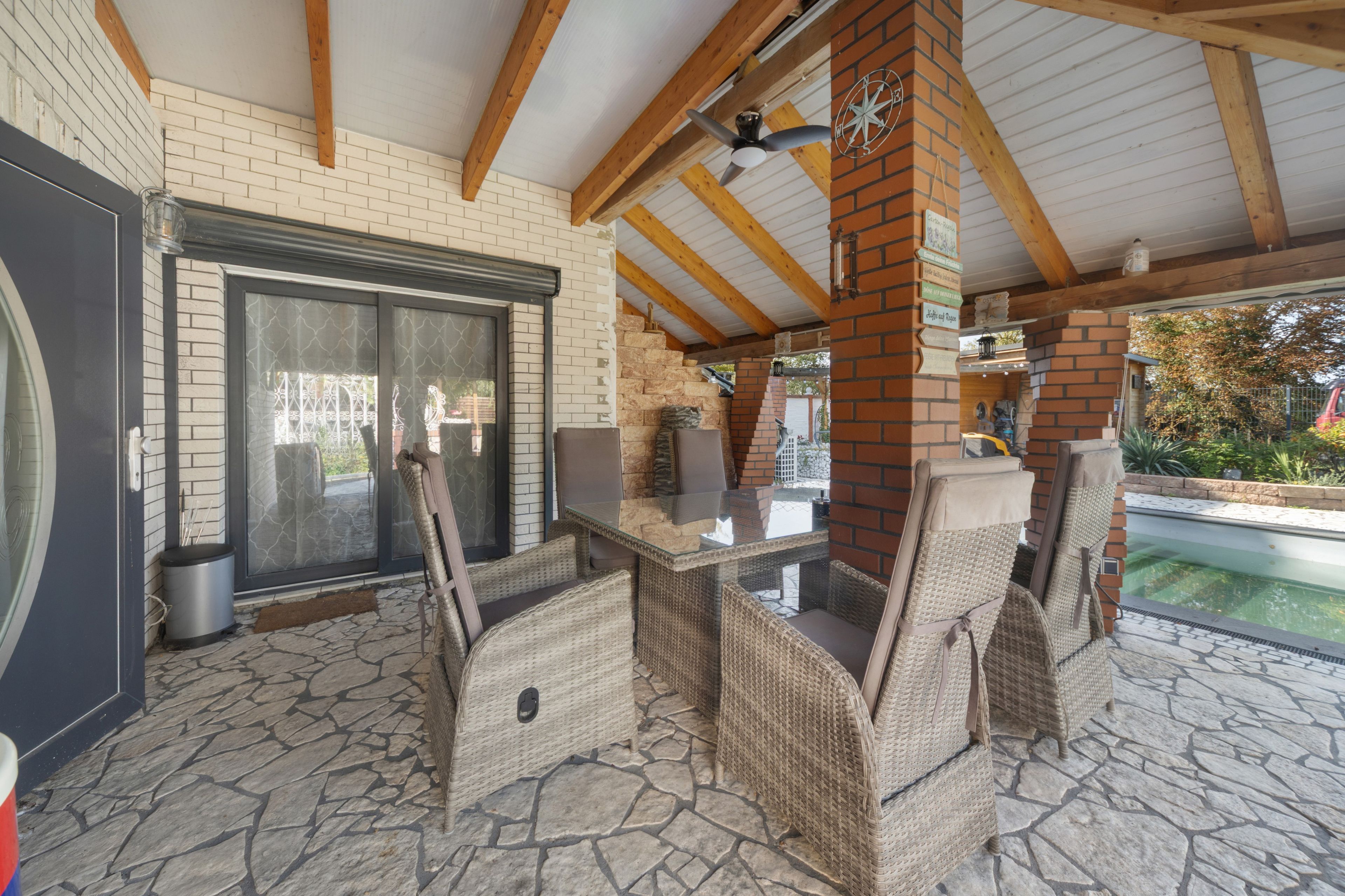Eine Außenpatio mit Steinboden, Korbmöbeln, einem Kamin aus Ziegeln und einem Pool im Hintergrund.