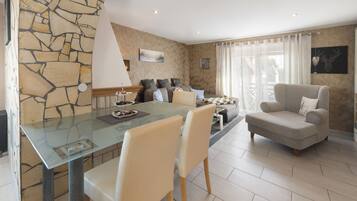 A modern living room with a glass dining table, beige sofas, and a stone accent wall.
