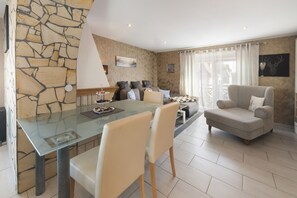 A modern living room with a glass dining table, beige sofas, and a stone accent wall. - Apartment 'Pooloase' with Pool, Terrace and Wi-Fi (Colbitz)
