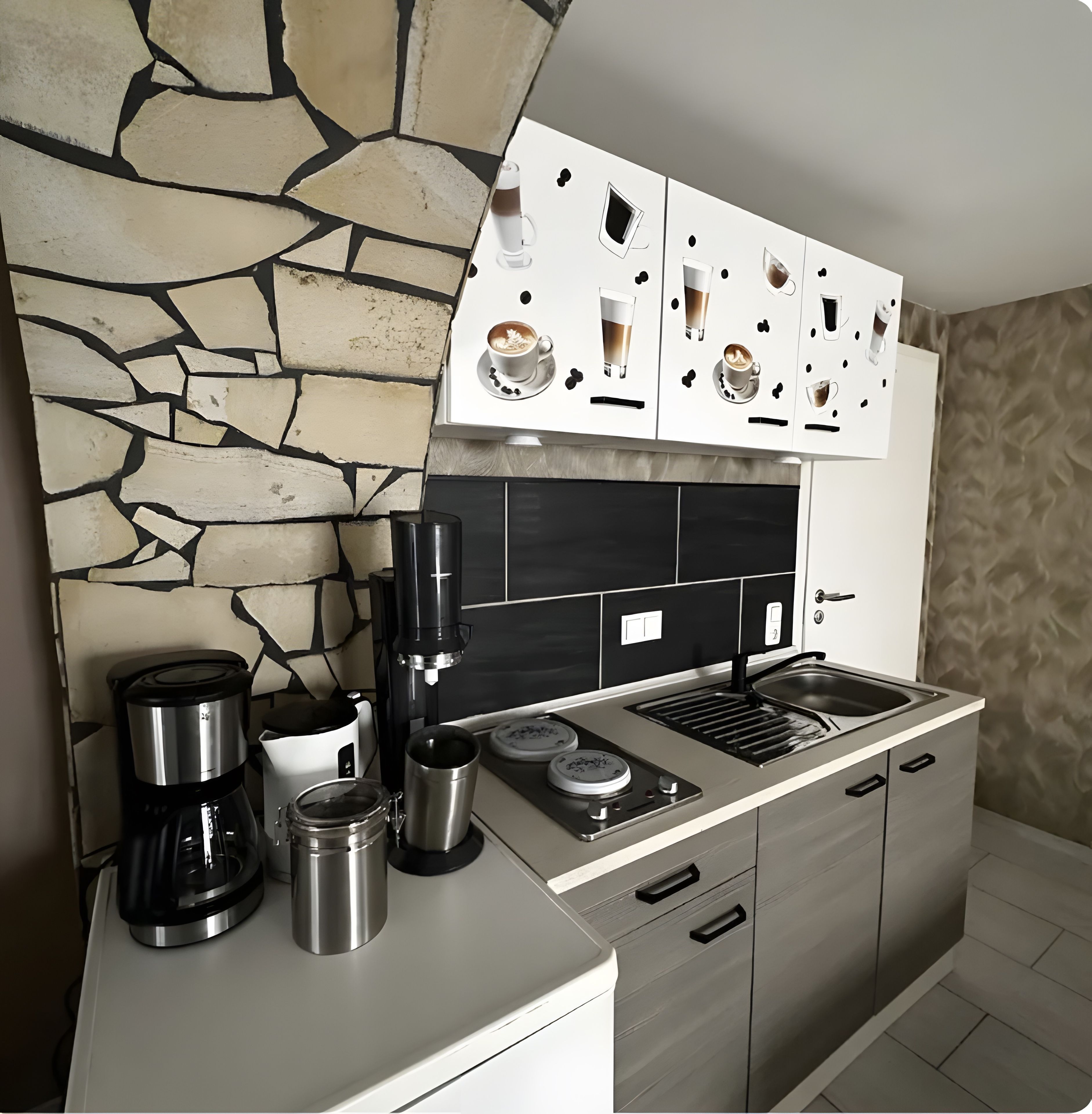 Eine moderne Küche mit Steinrückwand, einer Kaffeemaschine, einem Wasserkocher, einem Toaster und einem Spülbecken.