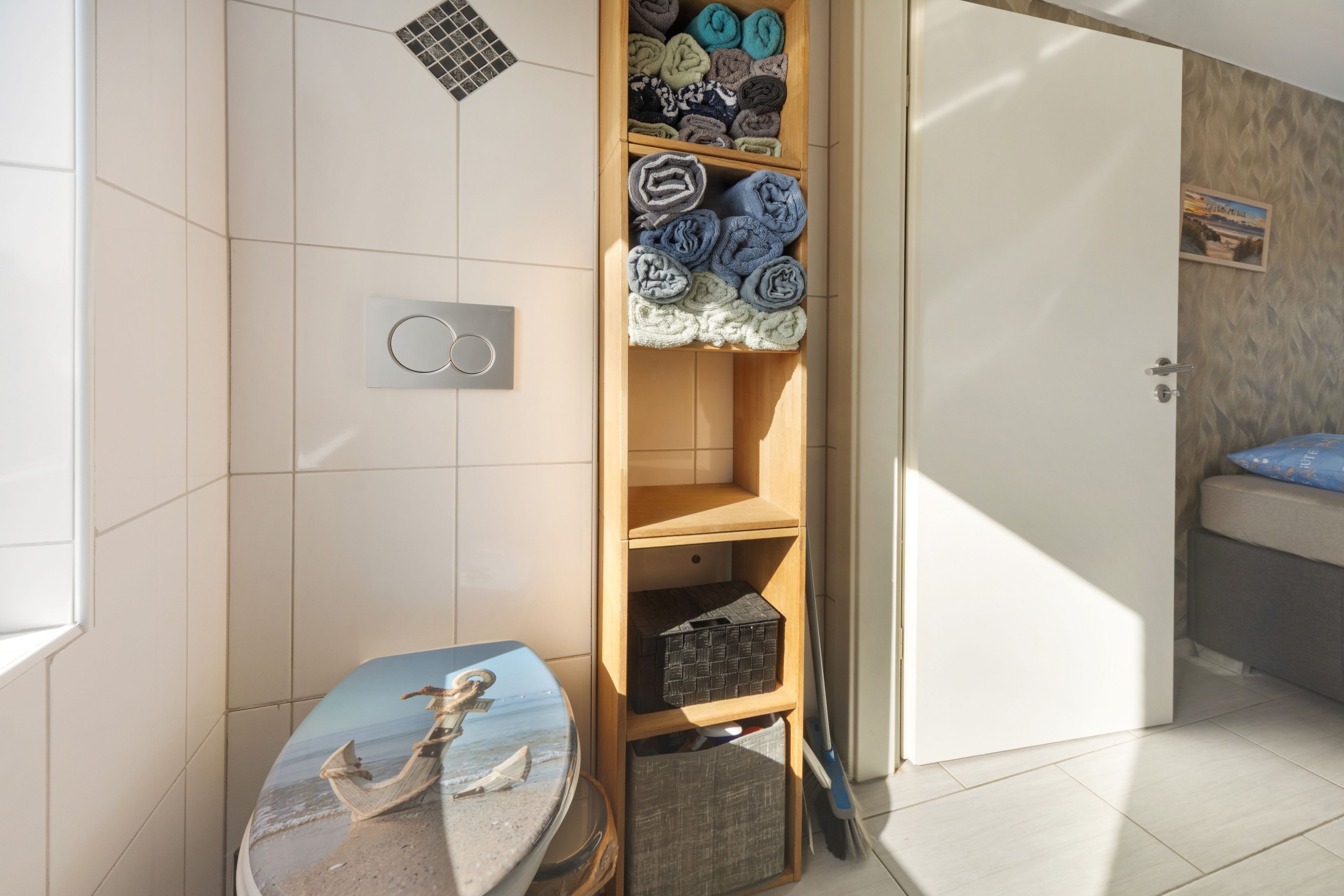 Ein Badezimmer mit Toilette, Ablagefläche mit Handtüchern, Duschbereich und einer Tür zu einem weiteren Raum.