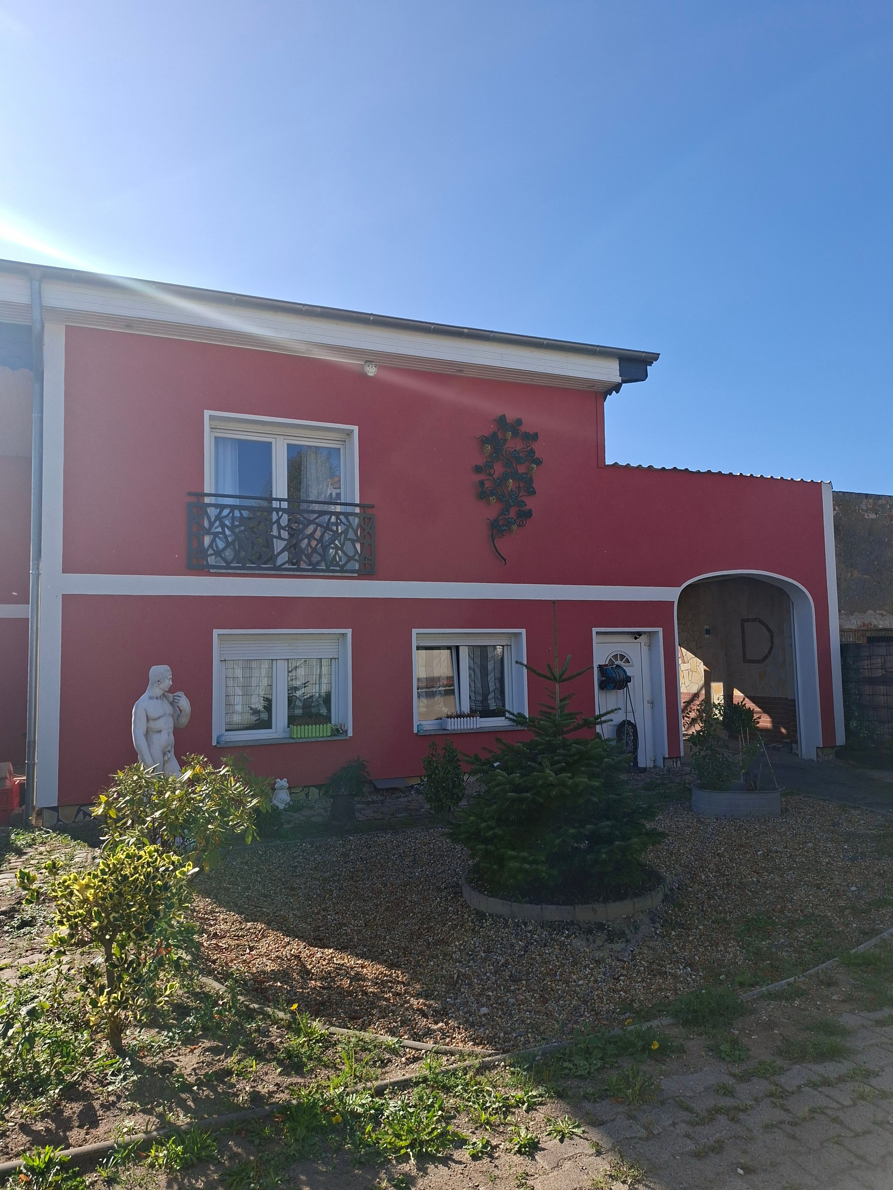 Un edificio rojo con una estatua, una letra 'D' en la pared y un camino de entrada de grava.