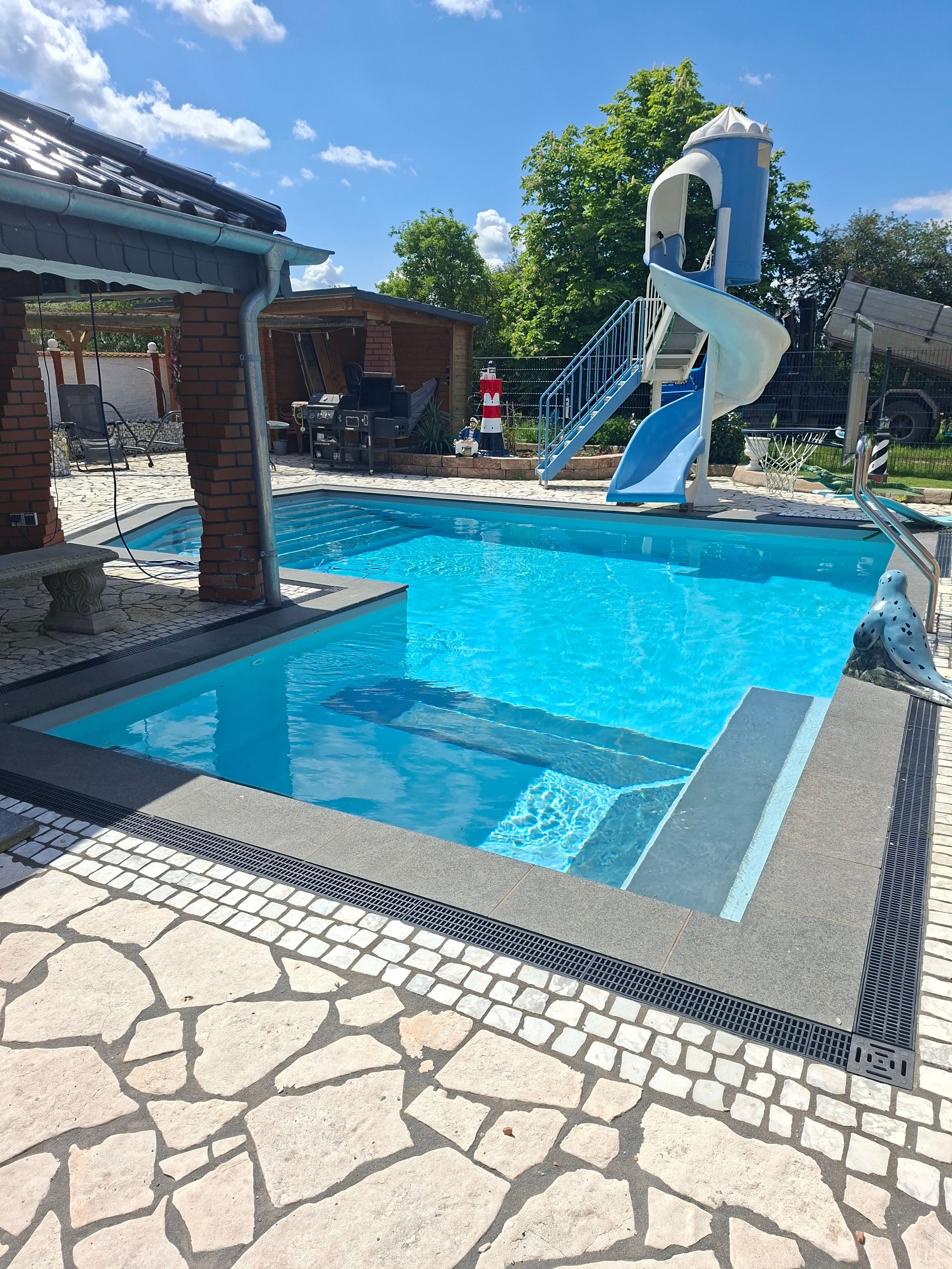 Una piscina con tobogán, baldosas de piedra y una estructura de ladrillo.