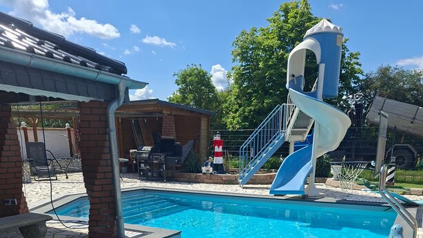 Una piscina con tobogán, baldosas de piedra y una estructura de ladrillo.