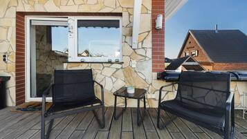 An outdoor patio with two black mesh chairs, a small table, and a stone wall with a welcome sign.
