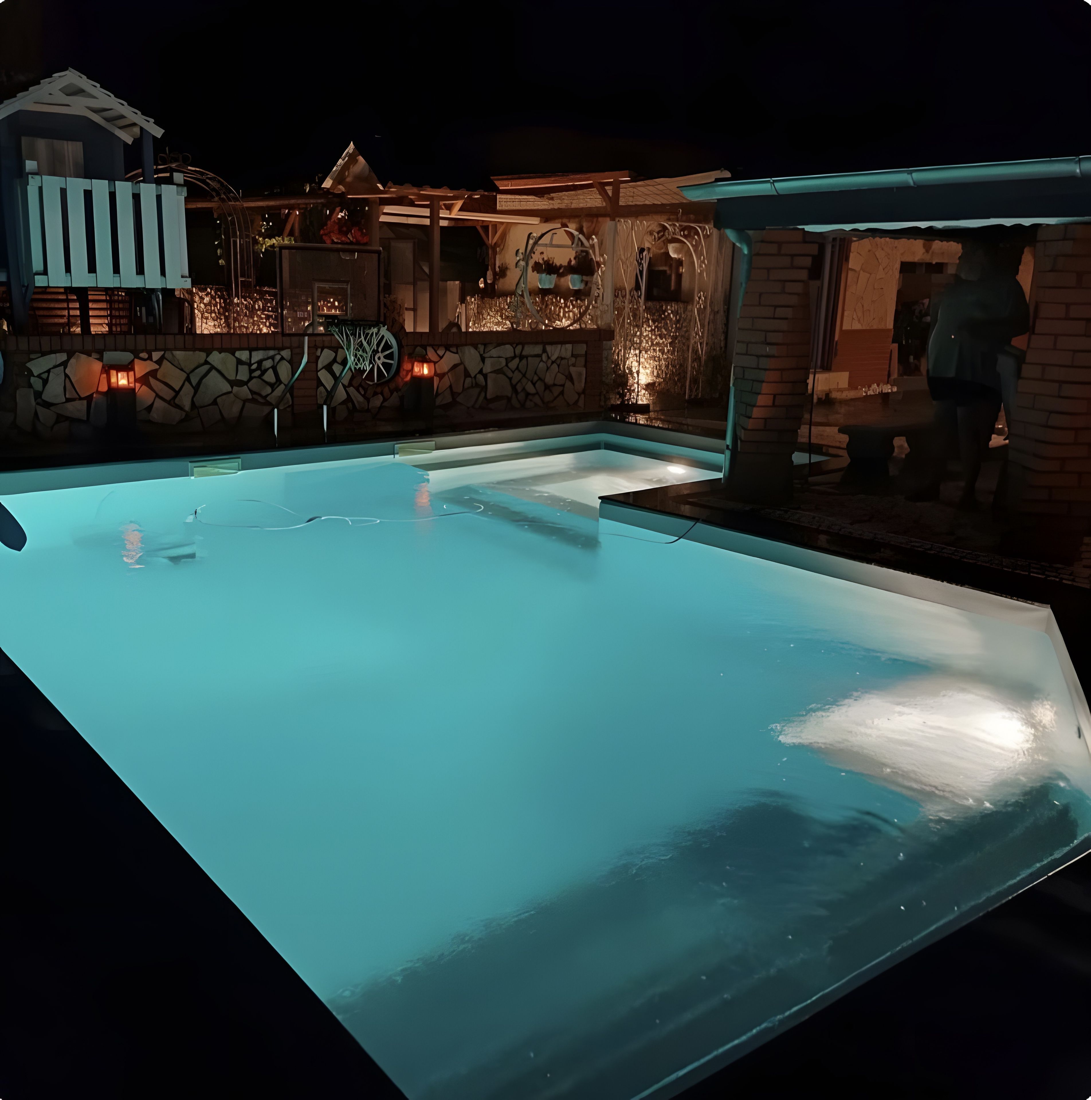 Una piscina con un muro de piedra y una zona cubierta con un banco.