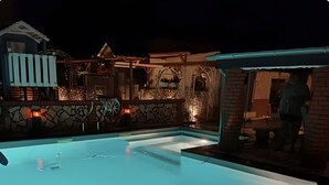 Una piscina con un muro de piedra y una zona cubierta con un banco.