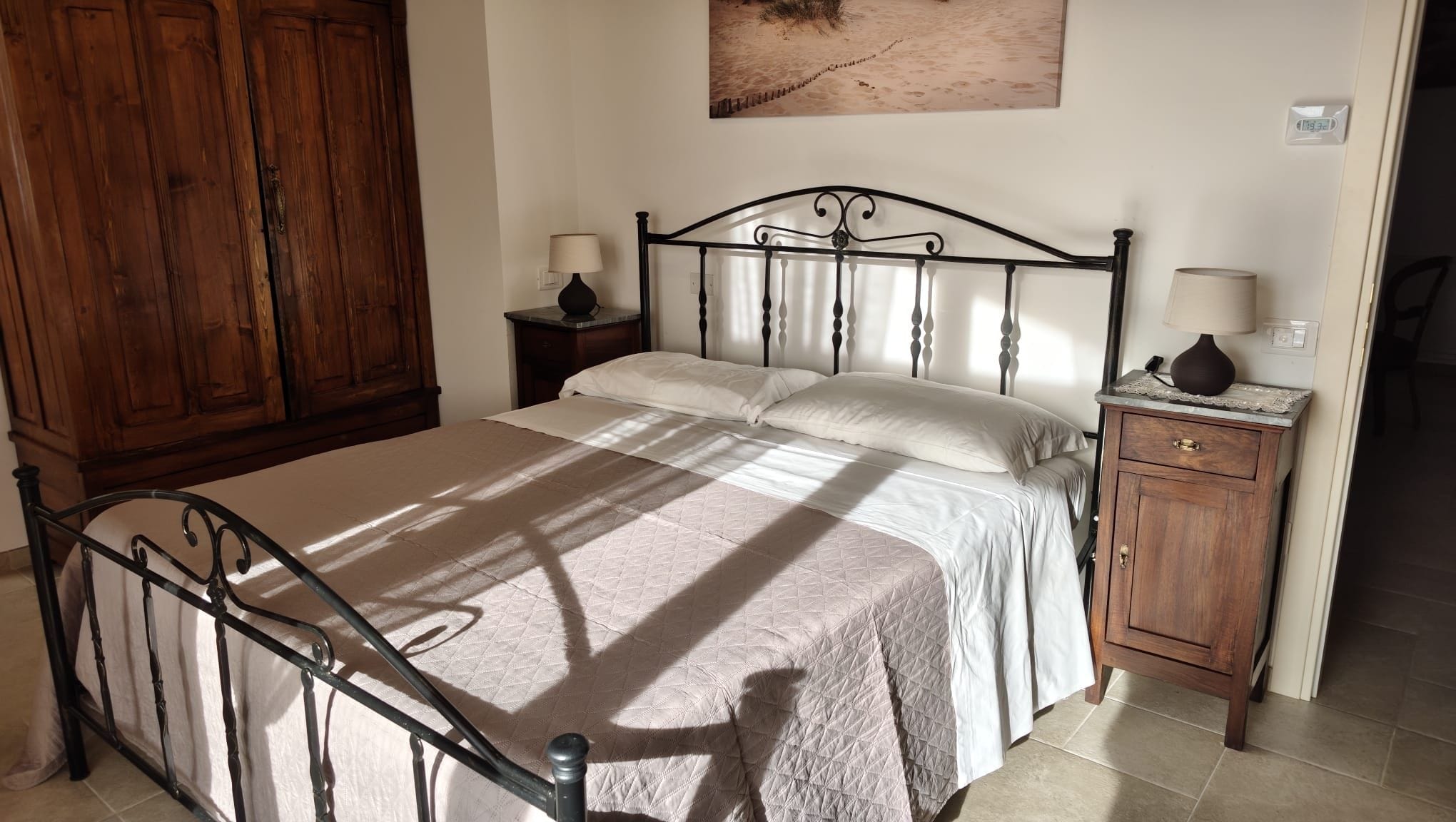 A bedroom with a bed, wooden wardrobe, bedside tables, and a wall-mounted lamp.