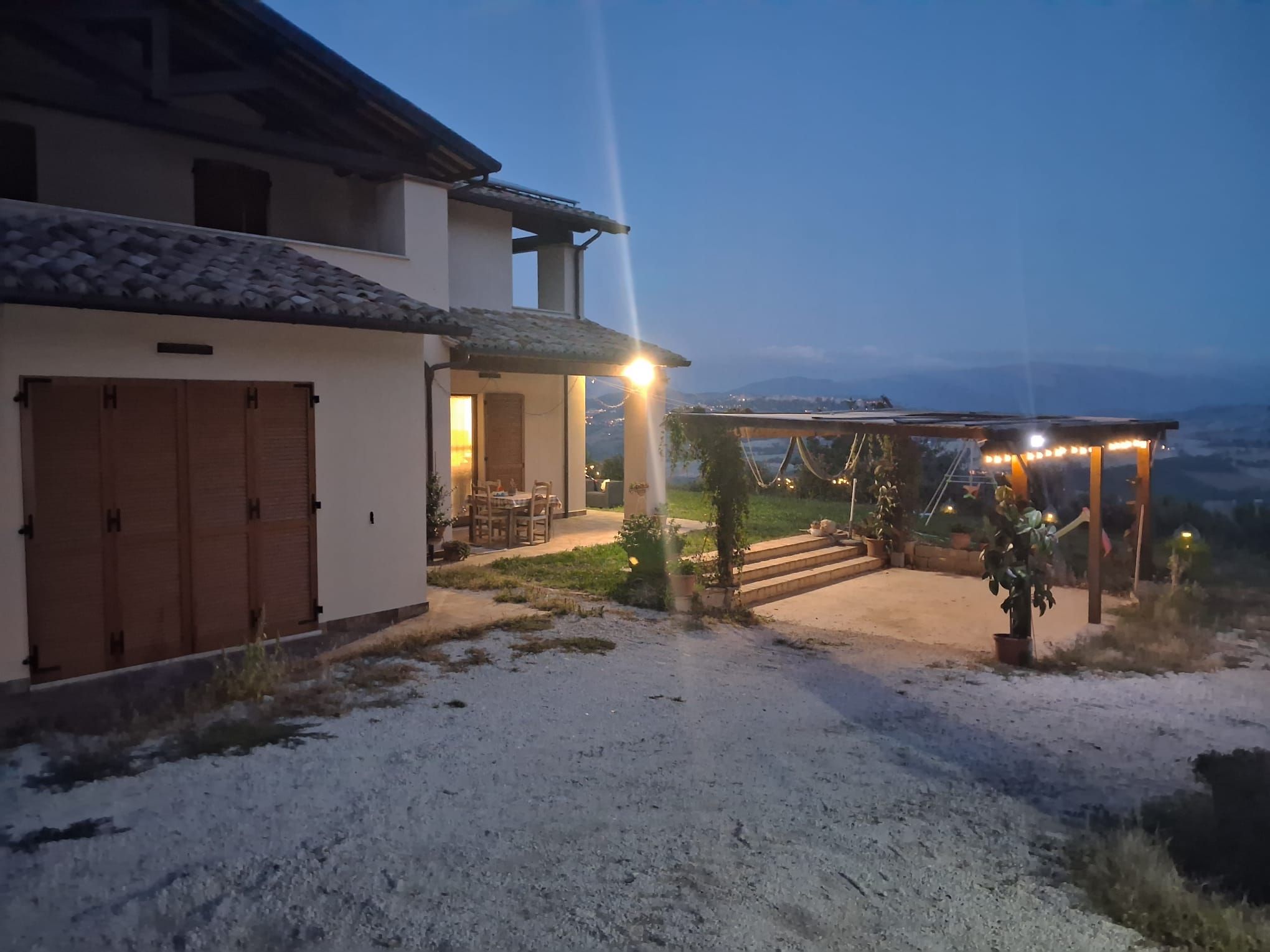 A building with a covered patio area, a gravel driveway, and a view of the landscape.