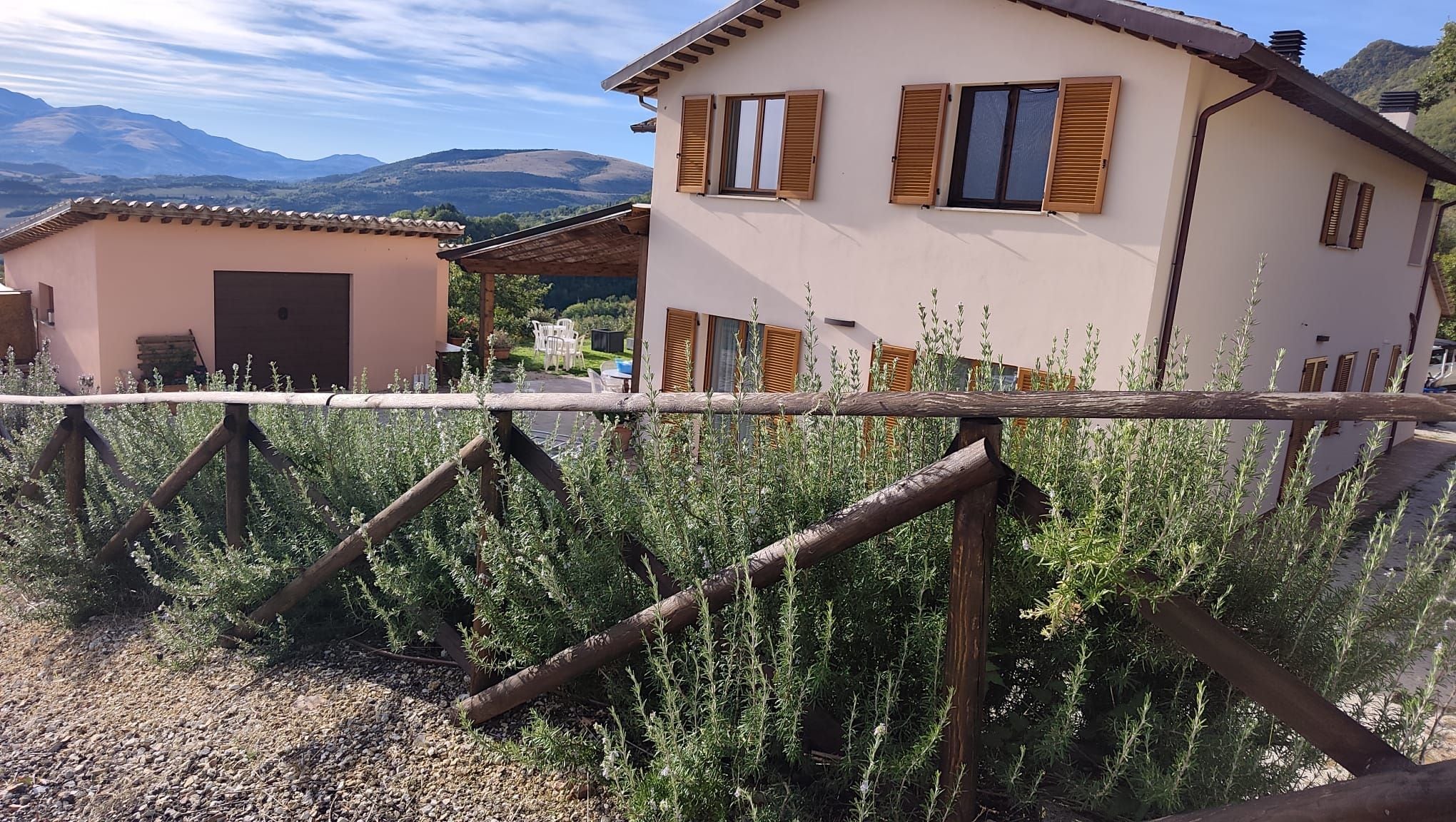 A house with wooden shutters, a gravel path, and a view of mountains in the background.