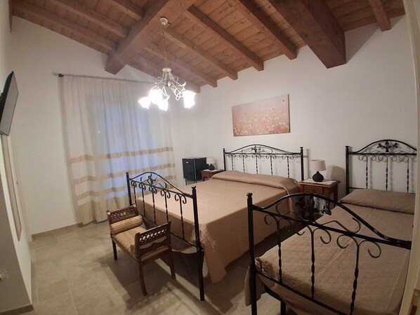 A bedroom with a wooden ceiling, a bed with a metal frame, a bedside table with a lamp, and a television on a stand.
