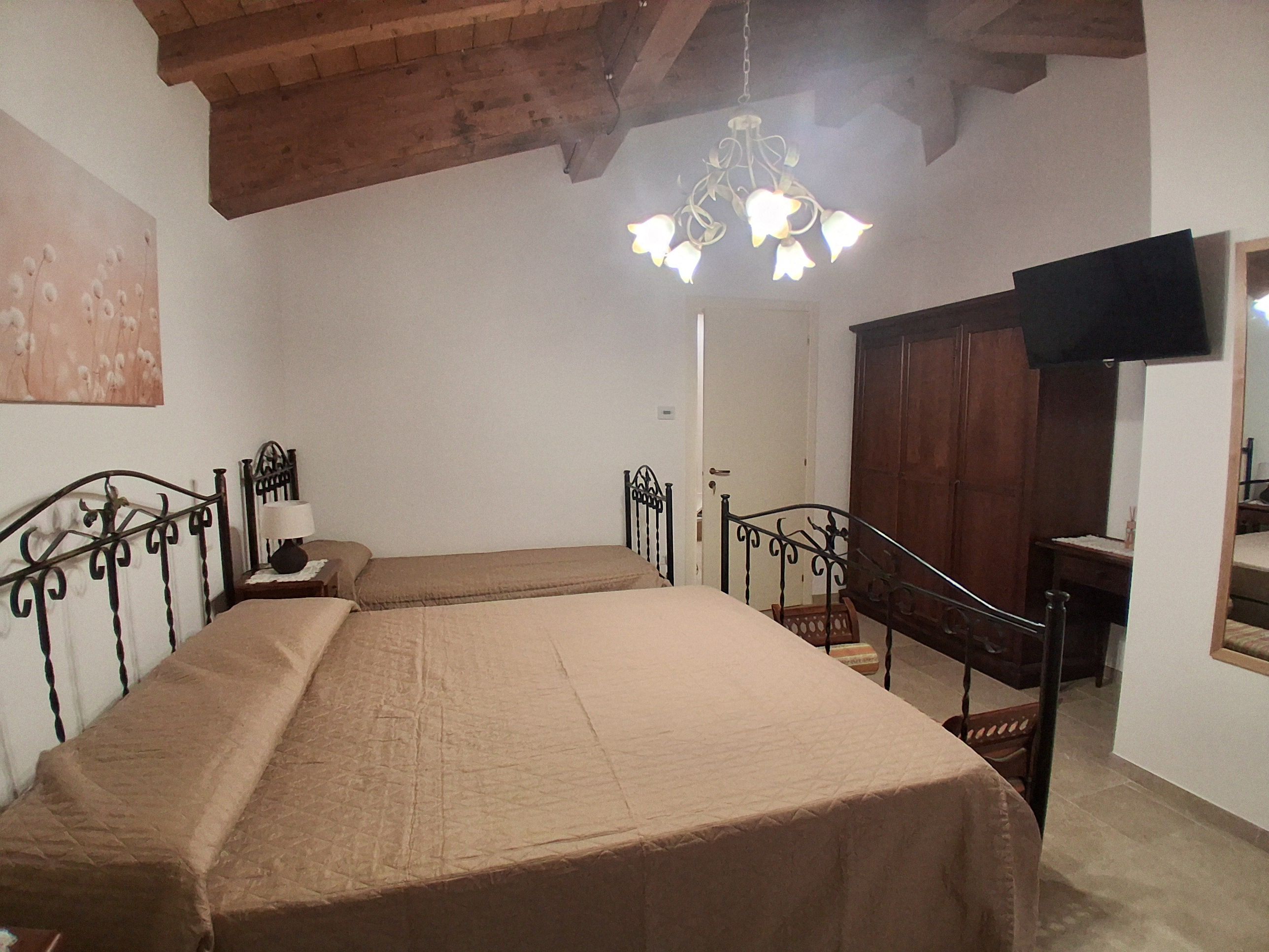 A bedroom with a double bed, a wooden ceiling, a chandelier, a wardrobe, and a television.