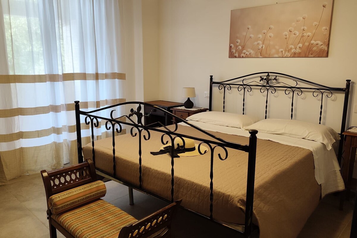 A hotel room with a bed, a chair, a nightstand, a lamp, and a painting on the wall.