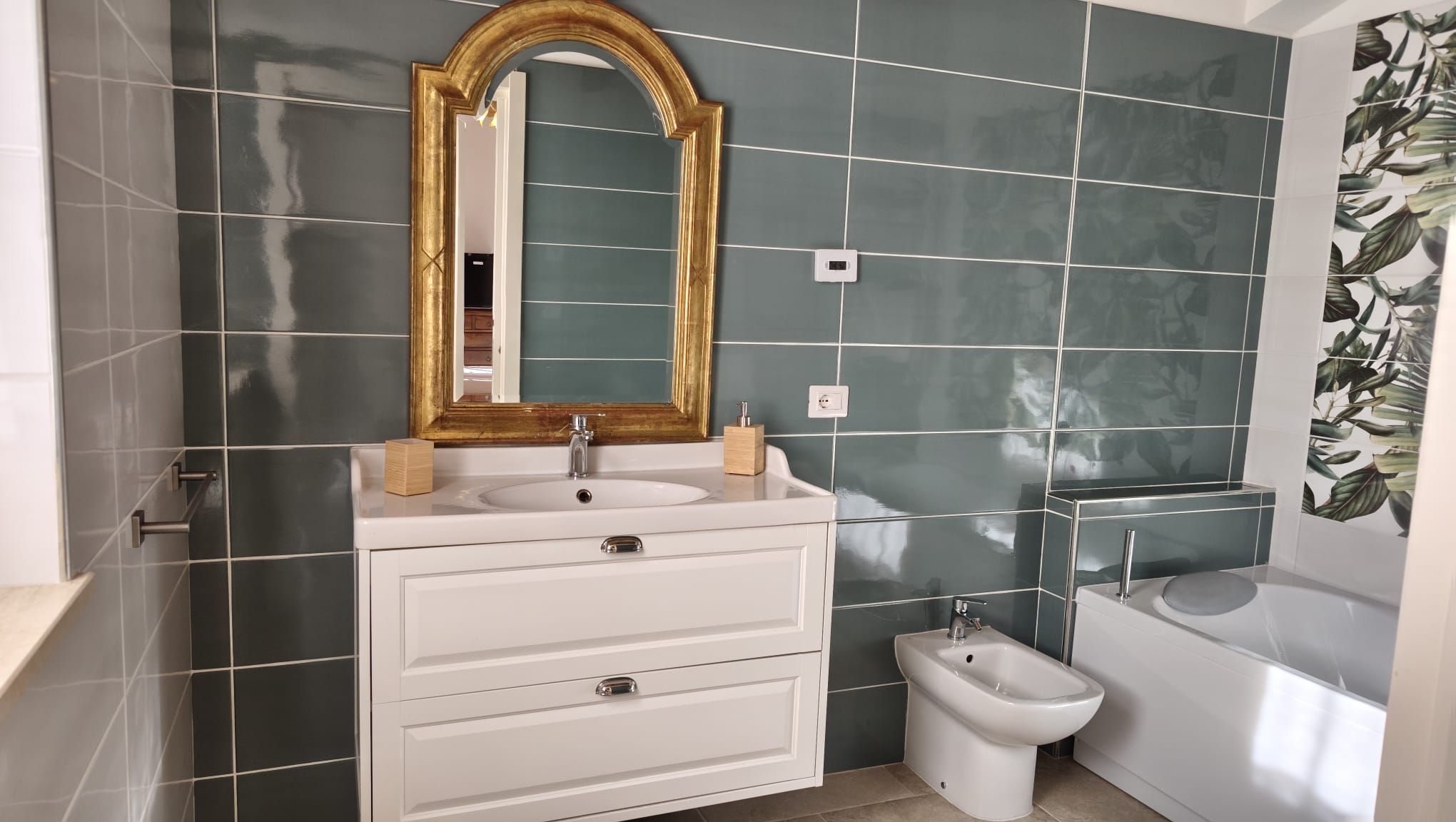 A bathroom with a white vanity, a gold-framed mirror, a bidet, and a bathtub.