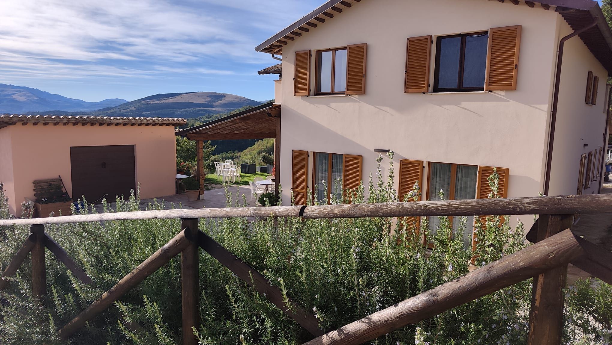 A two-story building with wooden shutters, a balcony, and a view of mountains.
