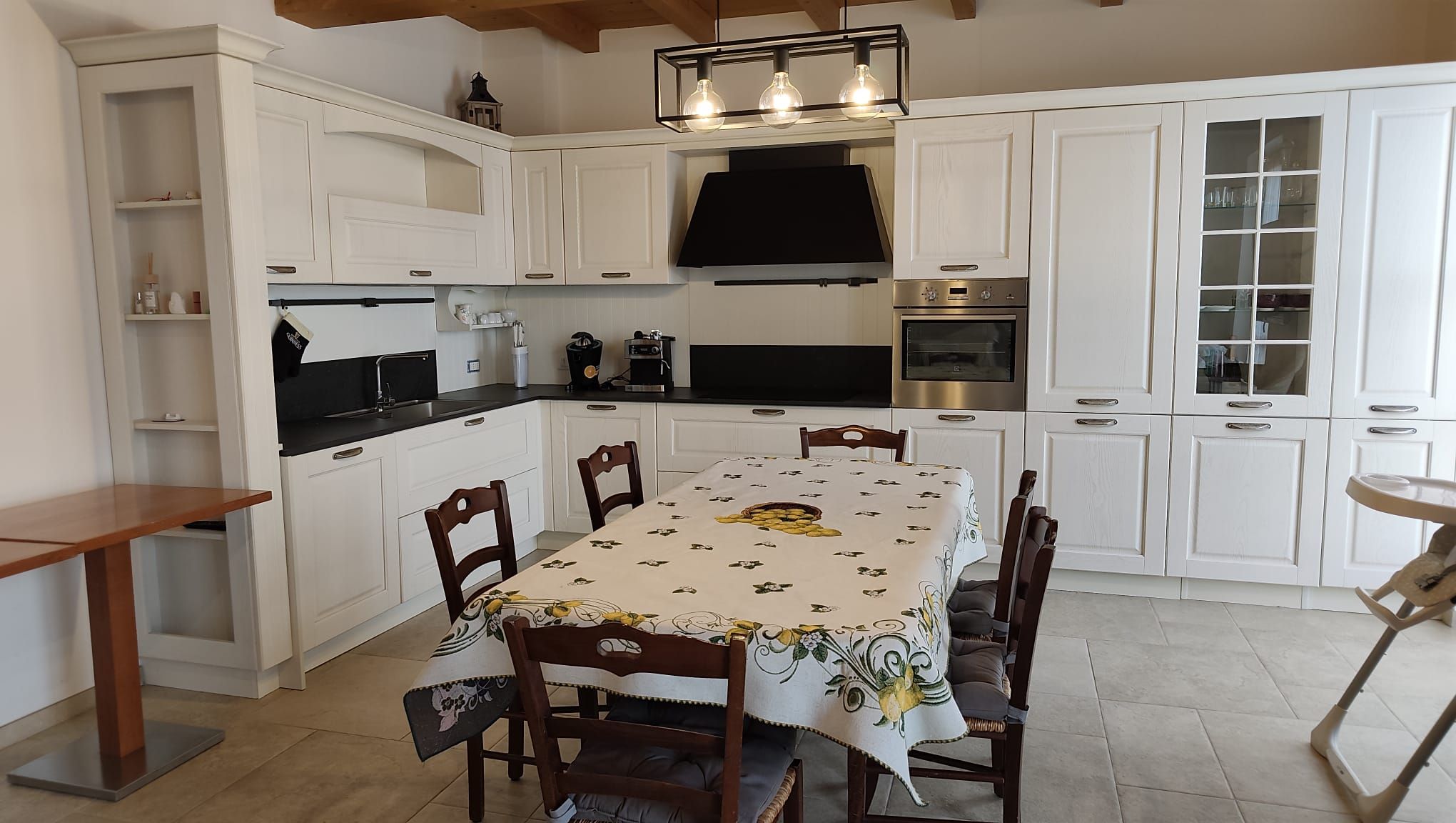 A kitchen with white cabinets, a black countertop, and a dining table with a floral tablecloth.