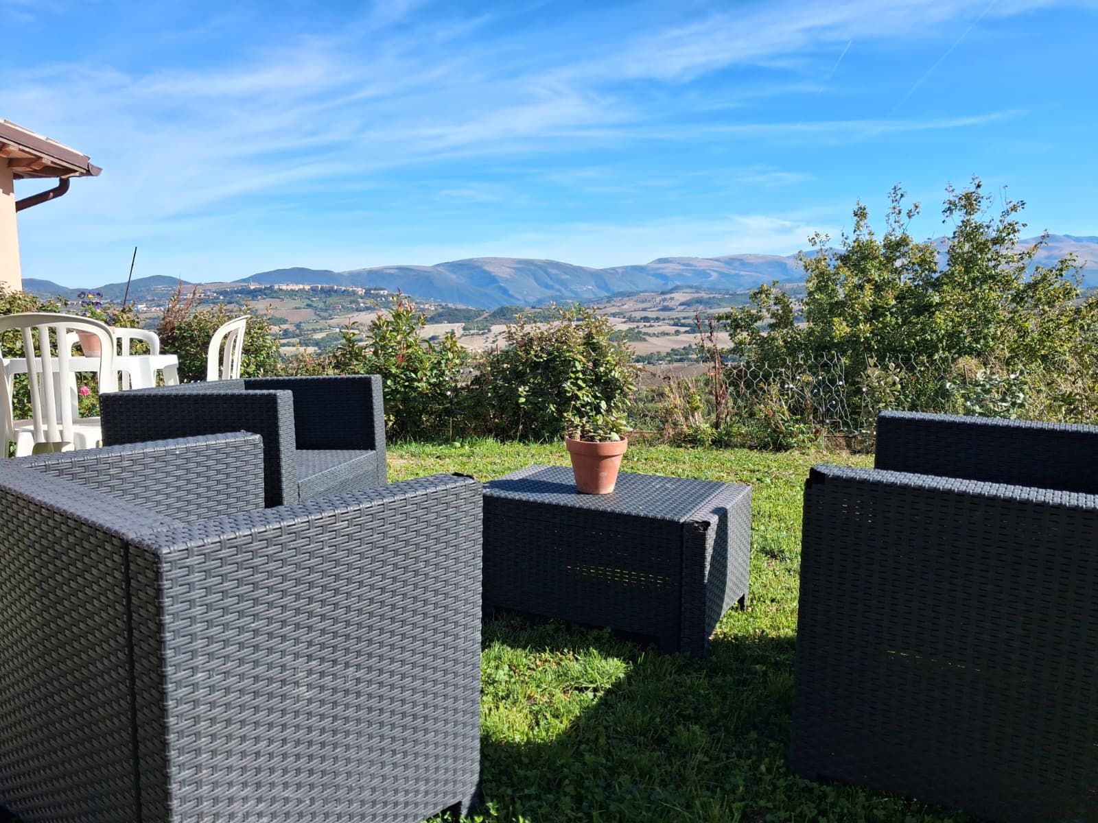 Outdoor wicker furniture arranged on a grassy area with a view of distant mountains and a clear sky.