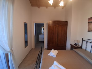 A bedroom with a bed, a wooden wardrobe, a nightstand with a lamp, and a bathroom visible through an open door. - Buon Vento (Camerino)
