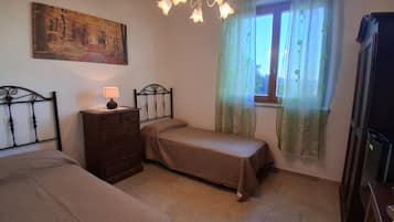 Une chambre avec deux lits, une commode, une lampe, un tableau au mur et une fenêtre avec des rideaux.