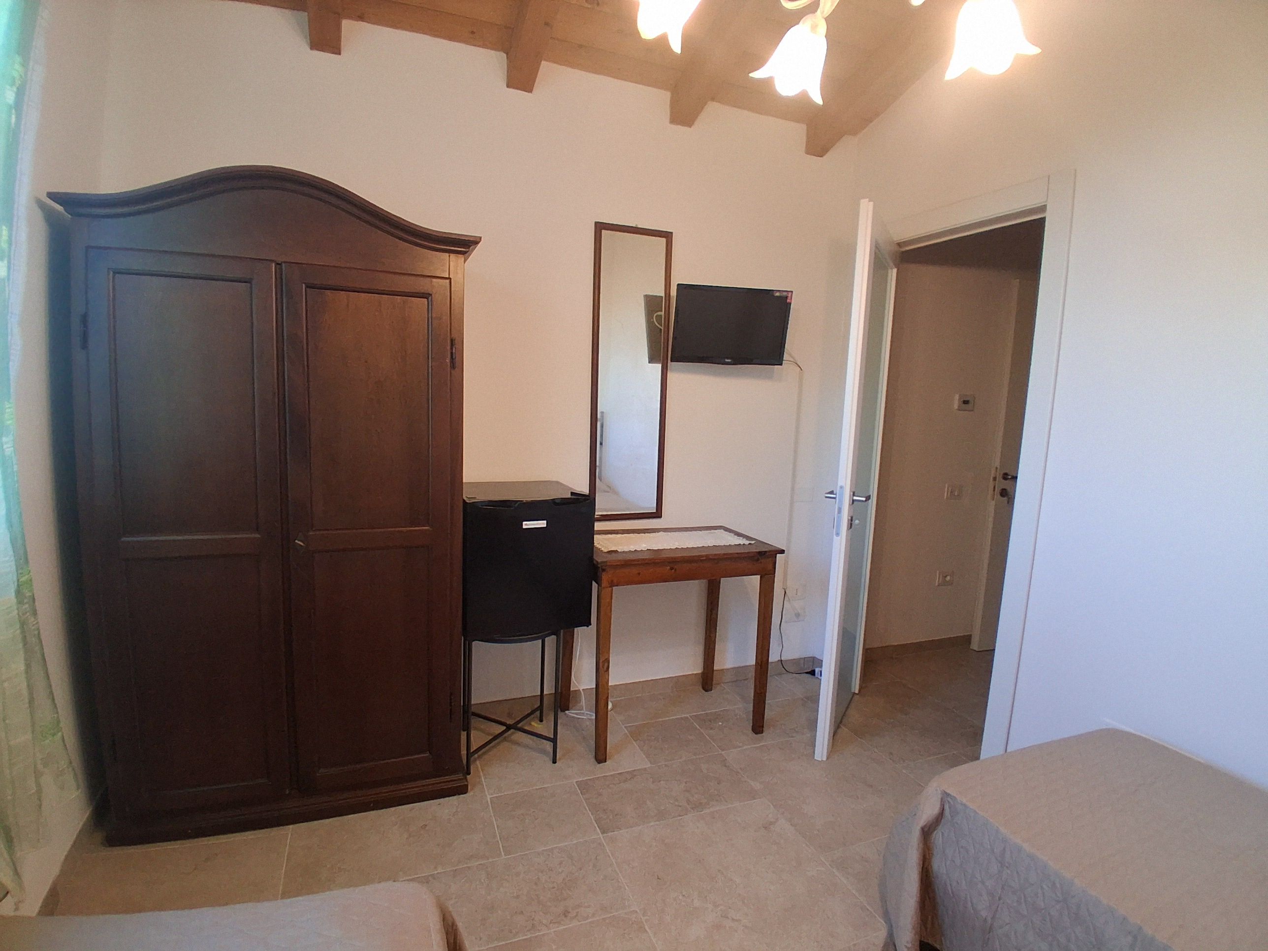 A room with a wardrobe, a desk, a mirror, and a door leading to another room.