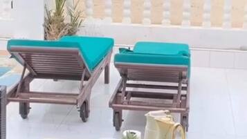 Een strandlounge met twee ligbedden, een tafel met fruit en gebak, en uitzicht op de oceaan.