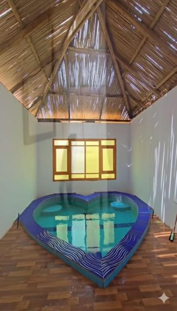 A room with a heart-shaped pool, a wooden ceiling, and a window with blinds.