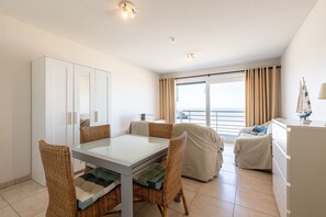 A hotel room with a balcony, a dining area with wicker furniture, and a view of the sea. - Studio Apartment With Sea Views in Gadeynehelling (Blankenberge)