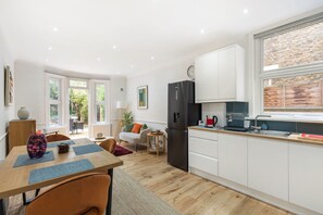 Eine moderne Küche mit weißen Schränken, einem schwarzen Kühlschrank und einem Fenster mit Blick auf eine Ziegelwand.
