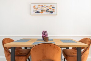 Ein Essbereich mit einem Holztisch, vier Samtstühlen, einer Vase und einem farbenfrohen, abstrakten Gemälde an der Wand.