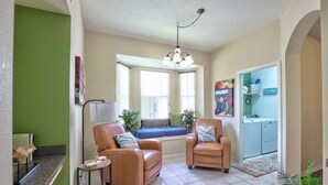 A living room with two leather chairs, a small table, a window seat, and a washing machine in the background. - Private Pool Paradise, Soaring Ceilings, Open Spaces & Fl Resort-Style Charm (Davenport)