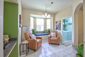 A living room with two leather chairs, a small table, a window seat, and a washing machine in the background. - Private Pool Paradise, Soaring Ceilings, Open Spaces & Fl Resort-Style Charm (Davenport)