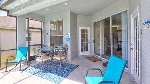 A covered patio area with a table and chairs, a door with a glass panel, and a view of the adjacent building. - Private Pool Paradise, Soaring Ceilings, Open Spaces & Fl Resort-Style Charm (Davenport)
