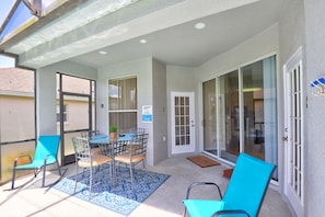 A covered patio area with a table and chairs, a door with a glass panel, and a view of the adjacent building. - Private Pool Paradise, Soaring Ceilings, Open Spaces & Fl Resort-Style Charm (Davenport)