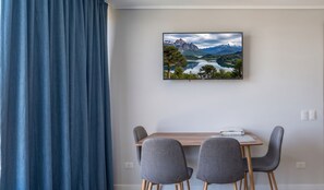 Ein Zimmer mit Esstisch, zwei Stühlen, einem Gemälde einer Berglandschaft und einem blauen Vorhang.
