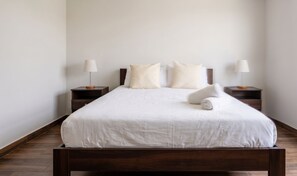 Un letto rifatto con lenzuola bianche, due comodini con lampade e un pavimento in legno.