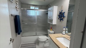A bathroom with a shower, toilet, sink, and a mirror with a ship's wheel decoration. - Shoreline Haven (Erie)