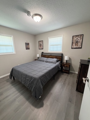 Une chambre à coucher comprenant un lit, des tables de chevet, une commode et une fenêtre avec des stores.