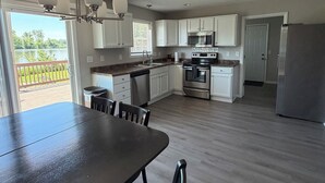 A spacious kitchen with white cabinets, a stainless steel refrigerator, and a dining area with a dark wooden table and chairs. - Shoreline Haven (Erie)